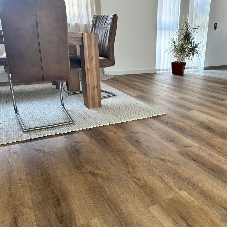 Eiche Eiche Apatura Klick-Vinylboden in Wohnzimmer mit Holztisch, Stühlen, Teppich und Pflanze