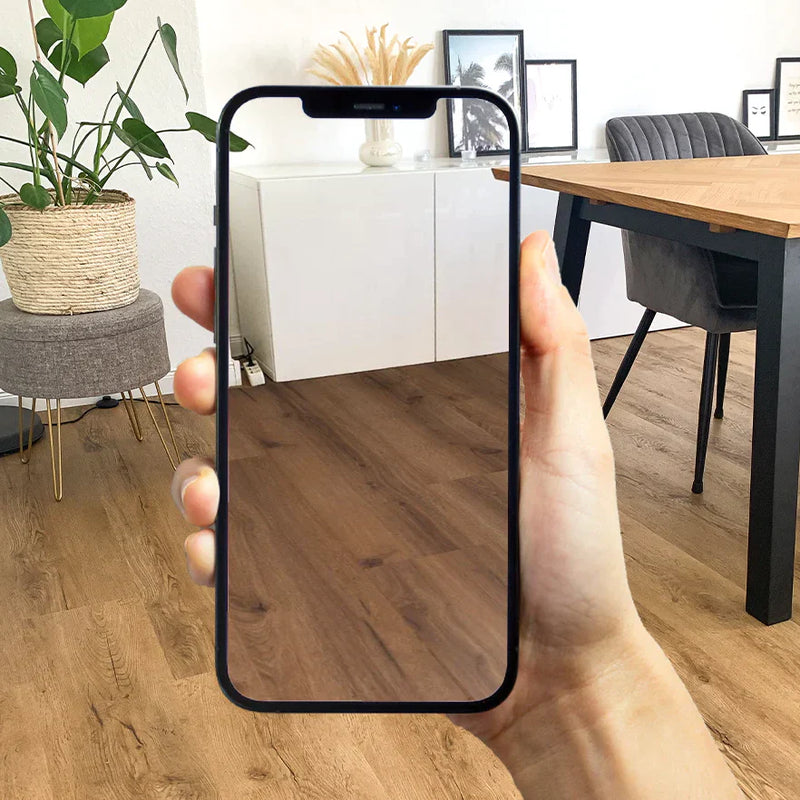 Ein Esszimmer in dem ein Holztisch steht und ein weißes Sideboard steht. Der Boden ist mit hellbraunem Klickvinyl verkleidet. Im Vordergrund ist ein Handy zu sehen auf dem der Raumplaner ausgeführt wird.