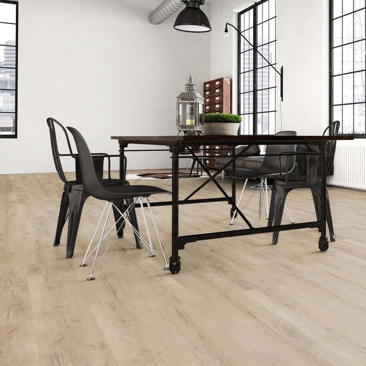 Industrial-Essbereich mit Klick-Vinylboden Eiche Fiducia in heller Holzoptik, schwarzem Metalltisch, Designstühlen und großen Loftfenstern – moderner Vinylboden von Laminatshop24